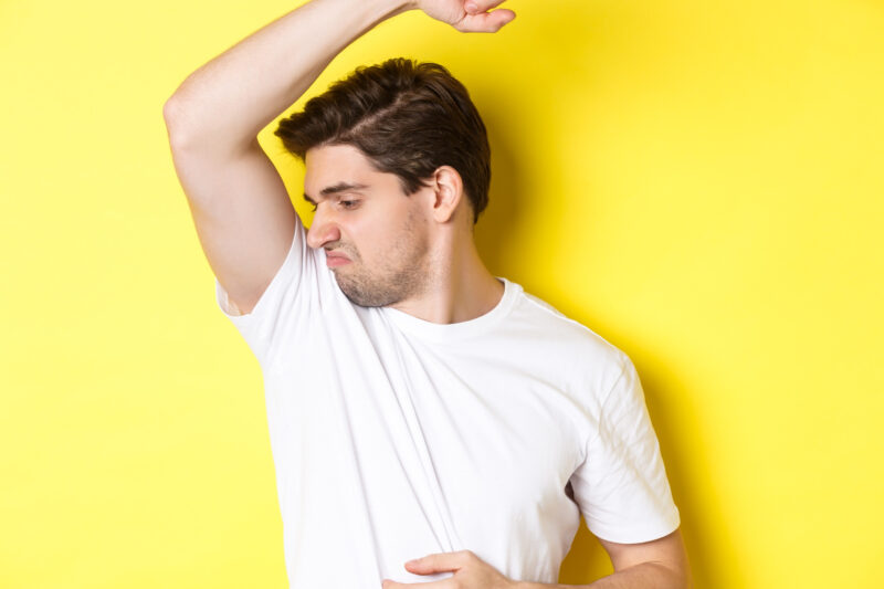 man sweat smelling his armpit standing white t shirt grimacing from stinky clothes