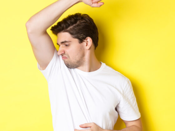 man sweat smelling his armpit standing white t shirt grimacing from stinky clothes