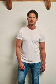 Man wearing a white basic T-shirt and jeans in front of a white wall.