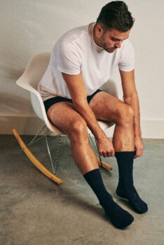 Man putting on dark socks from Suitable whilst sitting in a chair.